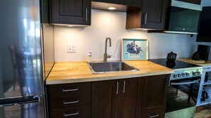 A modern kitchen with a stainless steel refrigerator, a double sink, wooden cabinets, and a microwave. - The MountainSide by Escapades Tremblant (Mont-Tremblant)