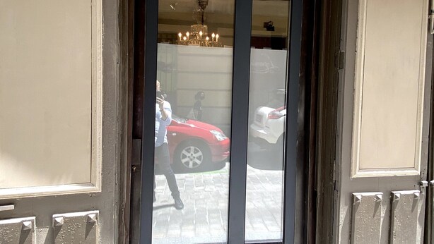 A door with a dark frame and a glass panel, leading to a building with a visible chandelier and parked cars outside. - Cozy Studio st Level in the Very Center of Madrid (Madrid)