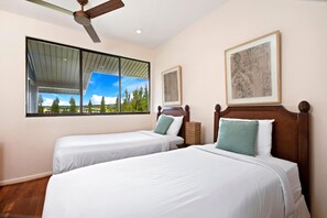 Une chambre avec deux lits, un ventilateur de plafond et une grande fenêtre donnant sur des arbres et un ciel dégagé.