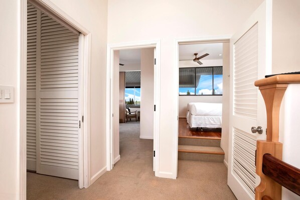 Un pasillo que conduce a un dormitorio con una cama, una silla y un ventanal con vista al cielo.