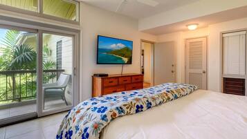 Una camera da letto con un letto, una cassettiera, un quadro e una porta vetrata scorrevole che dà su un balcone con piante.