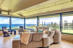Un salón amplio con un ventanal que ofrece vistas al océano y a los árboles.