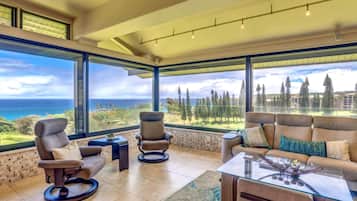 A spacious living room with a large view of the ocean and trees, modern furniture, and a high ceiling.