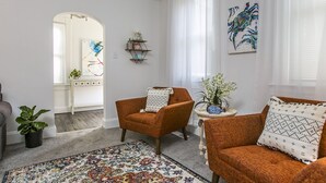 Un salón con un sofá, un sillón y una mesa de centro con una planta. Hay una alfombra en el suelo y un cuadro en la pared.