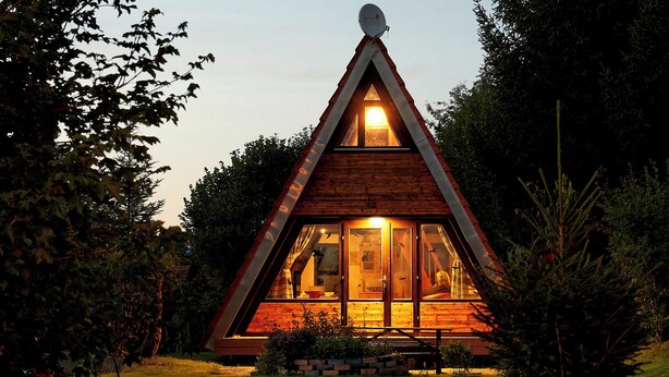 A wooden cabin with a triangular roof, large windows, and a satellite dish on the roof.