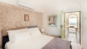 Ein Schlafzimmer mit Bett, Nachttisch, Wand-Klimaanlage und einer Tür zu einem Balkon mit Tisch und Stühlen.