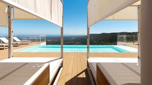 Ein Pool ohne Rand auf dem Dach mit weißen Liegestühlen und freiem Blick auf die Landschaft.