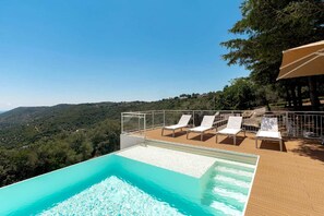 A pool with a clear view of the surrounding landscape, a wooden deck, and lounge chairs.