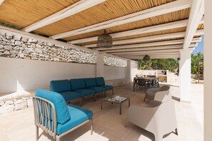An outdoor patio with a stone wall, a blue sofa, a white chair, and a dining table with chairs.