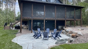 Una cabaña moderna de dos pisos con un patio de piedra y sillas Adirondack.