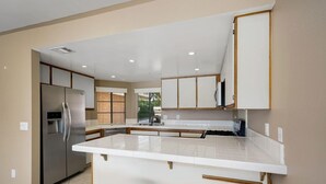 A modern kitchen with a stainless steel refrigerator, white countertops, and wooden stools. - Luxury Condo - Tranquil Desert Retreat  (Palm Desert)