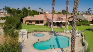 A residential area with a swimming pool, palm trees, and houses with red-tiled roofs. - Luxury Condo - Tranquil Desert Retreat  (Palm Desert)