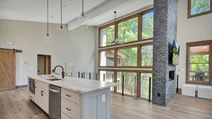 A spacious kitchen with a large island, wooden flooring, and a stone accent wall. - Watersong Falls ~ Private Waterfall, Hot Tub, Fire Pit & More (Ellijay)