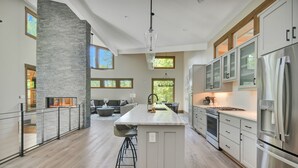 A modern kitchen with a central island, stainless steel appliances, and large windows. - Watersong Falls ~ Private Waterfall, Hot Tub, Fire Pit & More (Ellijay)