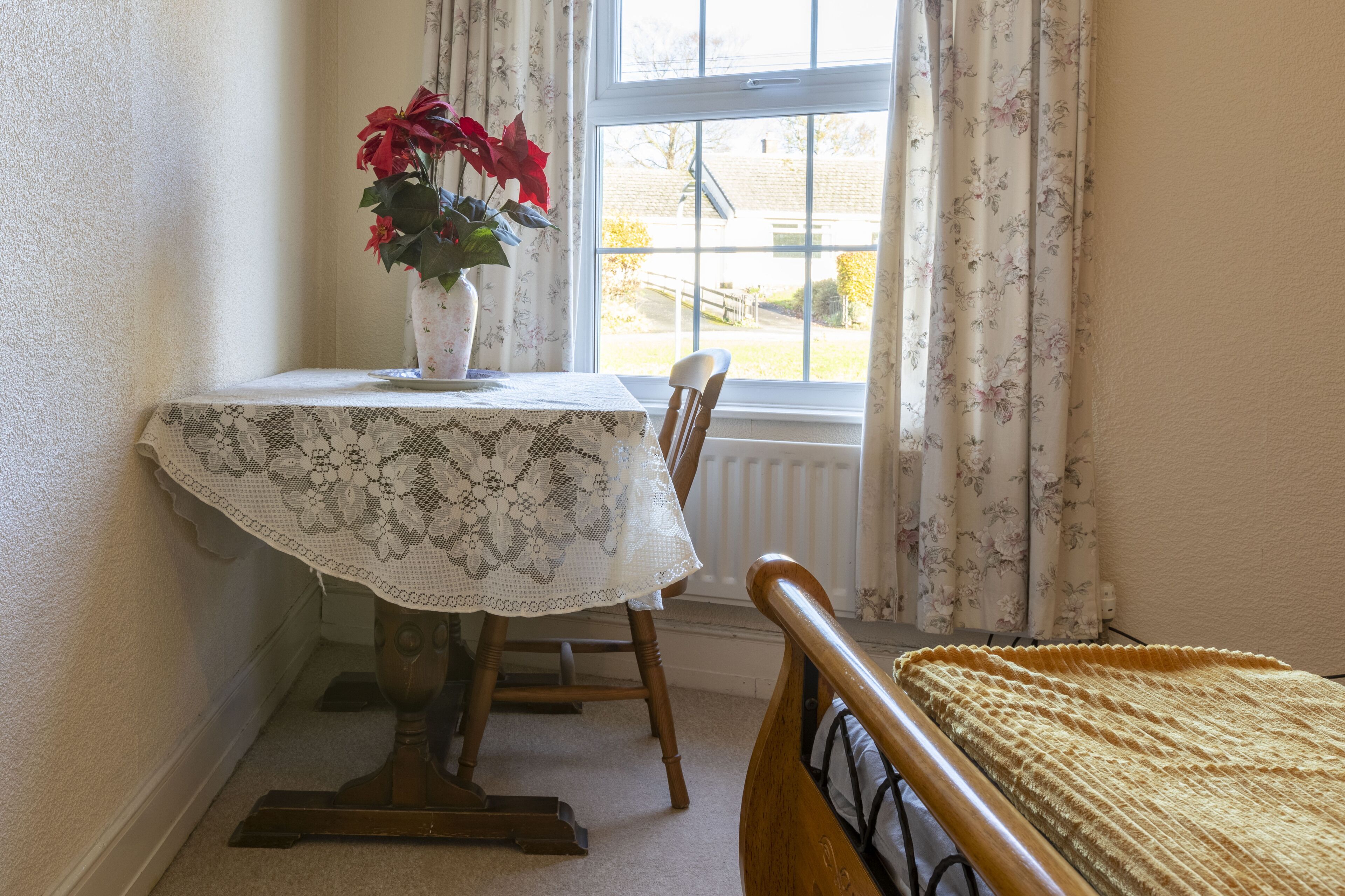 Una habitación con una mesa cubierta con un mantel de encaje, una silla de madera y una cama con una manta amarilla.