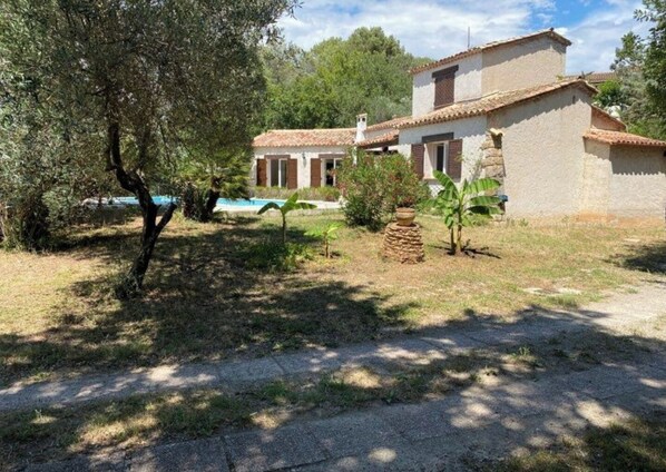 A rustic house with a stone facade, a tiled roof, and a small garden with a tree and a potted plant.
