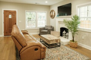 A living room with a brown leather sofa, a gray armchair, a wooden coffee table, a patterned rug, a fireplace, and a potted plant. - Welcome to Beltline (Atlanta)
