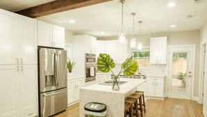 Una cocina moderna con armarios blancos, electrodomésticos de acero inoxidable, una isla de mármol y taburetes de madera.