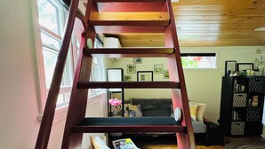 Un escalier en colimaçon en bois se trouve dans une pièce dont le sol est également en bois, et qui contient un canapé et une bibliothèque.