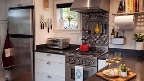 Une cuisine équipée d’un réfrigérateur en acier inoxydable, d’un grille-pain, d’une cuisinière et d’un plan de travail agrémenté d’une planche à découper, de verres à vin et d’une petite plante.