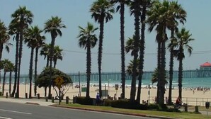 Ein Strand mit Palmen, einem Steg und einem Gebäude mit rotem Dach in der Ferne.