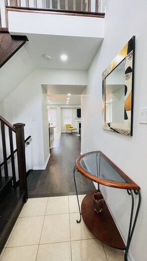 Un intérieur moderne avec un escalier, une table en verre et une chaise en cuir marron, ainsi qu’un miroir décoratif accroché au mur.