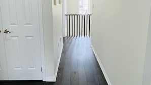A hallway with dark wooden flooring, white walls, and a white door on the left. - Beautiful detached 3 bedroom house,5 min from GO station. (Brampton)