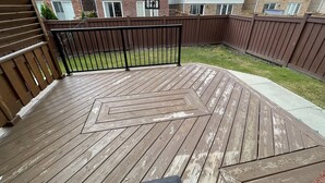 A wooden deck with a geometric pattern, surrounded by a brown fence and a brick building in the background. - Beautiful detached 3 bedroom house,5 min from GO station. (Brampton)