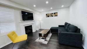 A living room with a flat-screen TV, a fireplace, a sofa, a yellow chair, and a coffee table. - Beautiful detached 3 bedroom house,5 min from GO station. (Brampton)