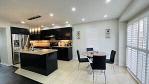 A modern kitchen with a central island, black cabinetry, stainless steel appliances, and a dining area with a glass table and chairs. - Beautiful detached 3 bedroom house,5 min from GO station. (Brampton)