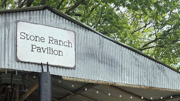Une construction rustique en pierre, portant l’inscription « Pavillon Stone Ranch », avec un toit en métal, et entourée de verdure.