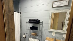 Une salle de bain avec des toilettes, une étagère avec des serviettes, un miroir et un panneau au-dessus du miroir.