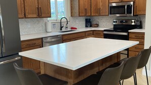 Une cuisine moderne avec des meubles en bois, un réfrigérateur en acier inoxydable, un four à micro-ondes, un four traditionnel et un grand îlot central doté de tabourets de bar.