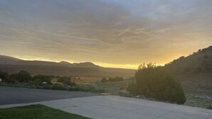 Un quartier résidentiel avec une allée pavée, une pelouse verdoyante et une vue sur les montagnes lointaines au coucher du soleil.
