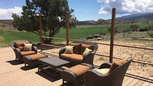 Une terrasse dotée de meubles en osier et offrant une vue sur un champ verdoyant et des montagnes.
