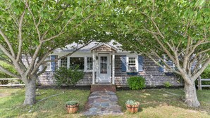 Une maison avec un chemin de pierre menant à la porte d’entrée, entourée d’arbres et agrémentée de deux jardinières avec des plantes.