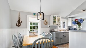 Une cuisine avec une table et des chaises en bois, des armoires blanches et un luminaire suspendu.