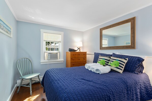 Un dormitorio con una cama grande, un aparador de madera, una silla y una ventana con persianas.