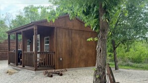 Une cabane en bois rustique avec un porche, une enseigne indiquant « Meadowlark », et un vélo appuyé contre un arbre.