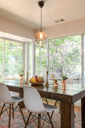 Un espace repas avec une table en bois, des chaises blanches et un luminaire suspendu.