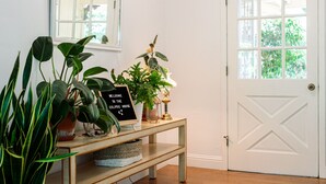 A hallway with a white door, a console table with plants, a welcome sign, and a light fixture. - The Eclipse House: Escape to the Trees (Nevada City)