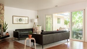 A modern living room with a black leather sofa, a small wooden table, and a potted plant. - The Eclipse House: Escape to the Trees (Nevada City)