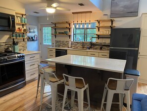 Una cocina moderna con una isla central, taburetes de bar, un microondas, una estufa y un refrigerador.