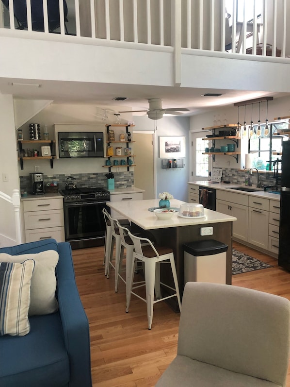 Una cocina moderna con una isla central, armarios blancos y una zona de comedor con un sofá azul y sillas blancas.