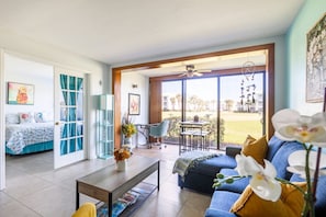 Relax in this open-plan living space with a sofa, dining table, and comfortable bed, leading to a serene outdoor area.