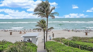 A beach with palm trees, lounge chairs, and a pathway leading to a building.