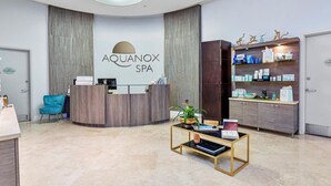A reception area with a reception desk, a blue chair, a coffee table with a book, and a shelf with products.