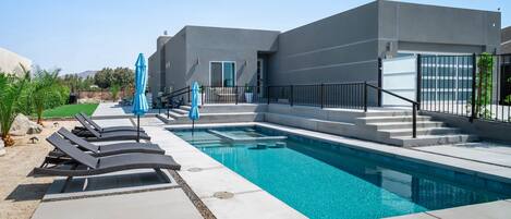 Un espace piscine extérieur moderne, doté de chaises longues et de parasols, d’un escalier menant à un bâtiment et d’un ciel dégagé.