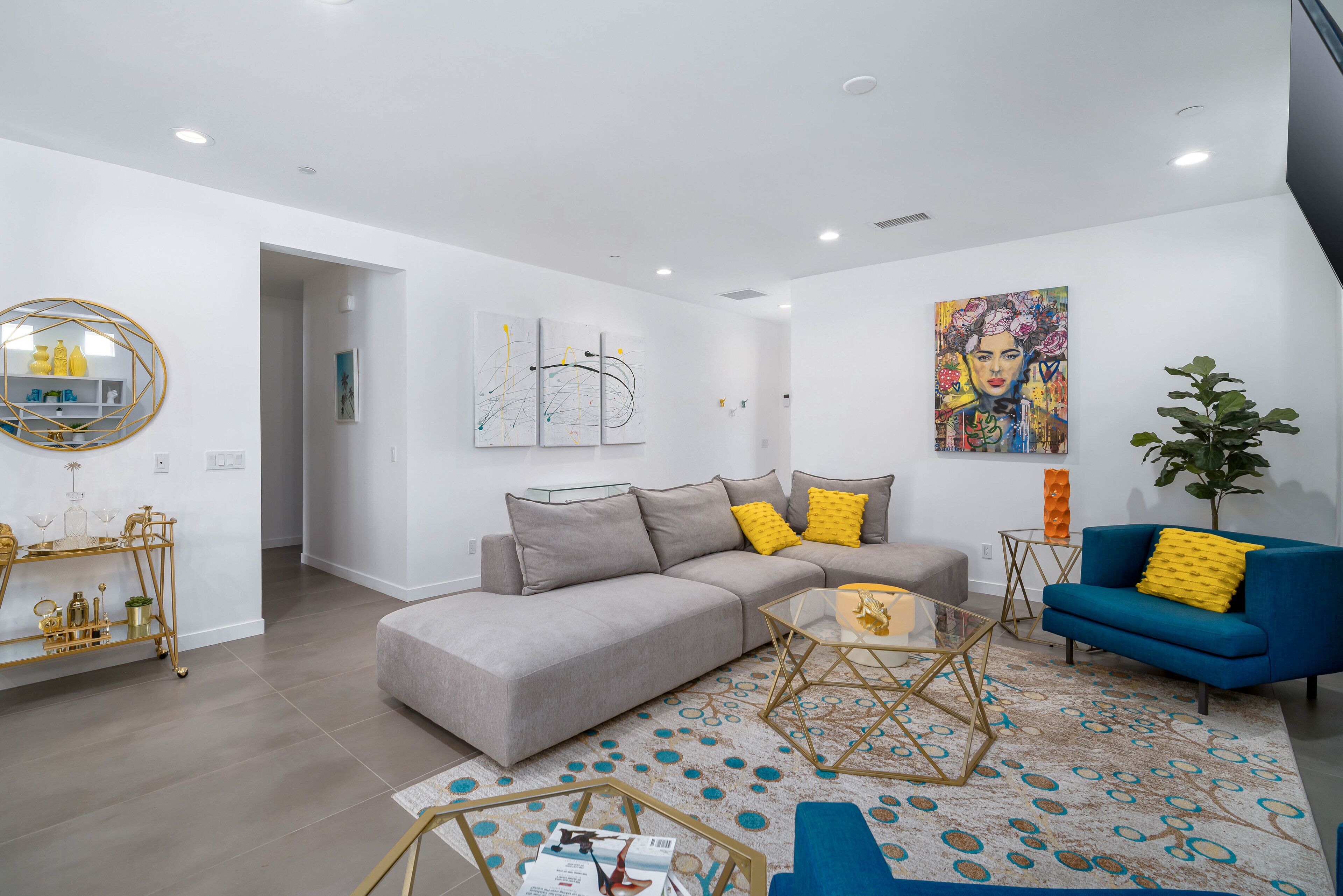 A modern living room with a grey sofa, blue armchair, and a coffee table. There is a gold-framed side table and a decorative wall piece.