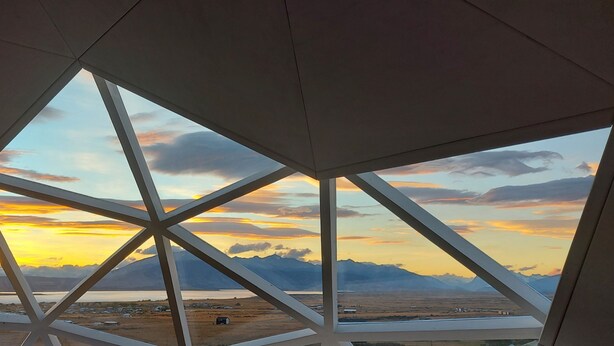 A view through a geometric window structure with a sunset and mountains in the background. - Geodesic Dome with Stunning Glacier and Mountain views (Puerto Natales)